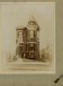 Sepia photograph of a tall, ornate Victorian-style house with a steep gabled roof, bay windows,…