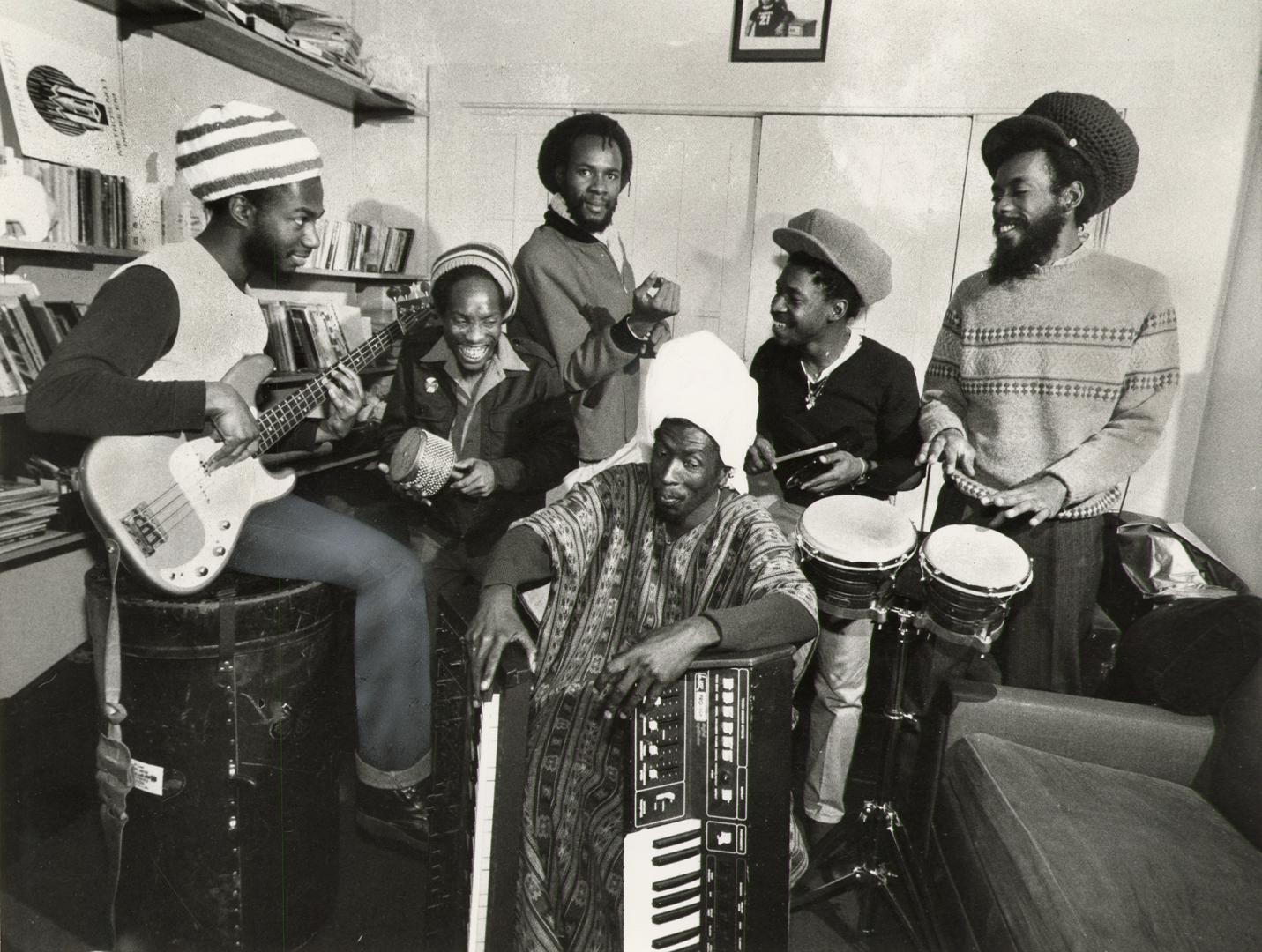 A reggae band of 6 smiling Jamaican men, holding their instruments with joy