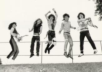 5 young men jump up into the air in front of iron fence. They wear black tights and leopard pri…