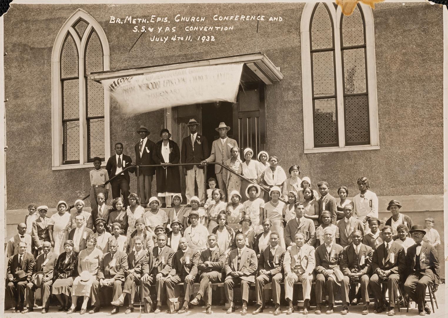 Black-and-white group photograph of several dozen people posed on the steps and in front of a s…