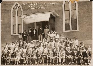 Black-and-white group photograph of several dozen people posed on the steps and in front of a s…