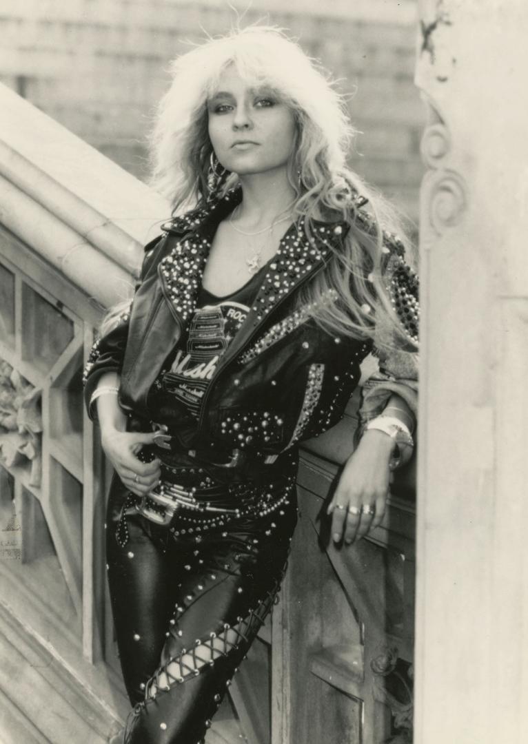 Woman with long blond hair wearing black leather studded clothing beside on bridge..