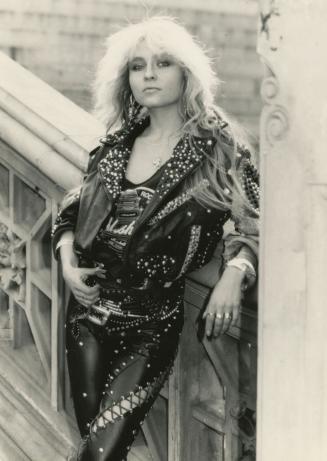 Woman with long blond hair wearing black leather studded clothing beside on bridge..