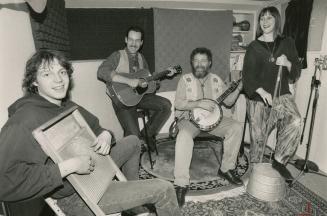In a room with Persian carpet on floor, young man with washboard, man with acoustic guitar, nex…