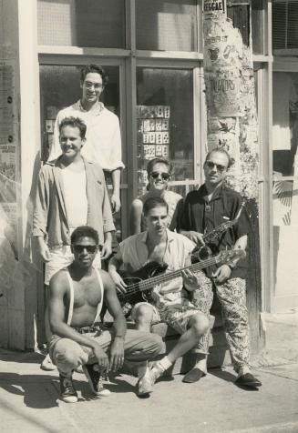 Outdoors, day, 5 men and one woman crowd around a storefront