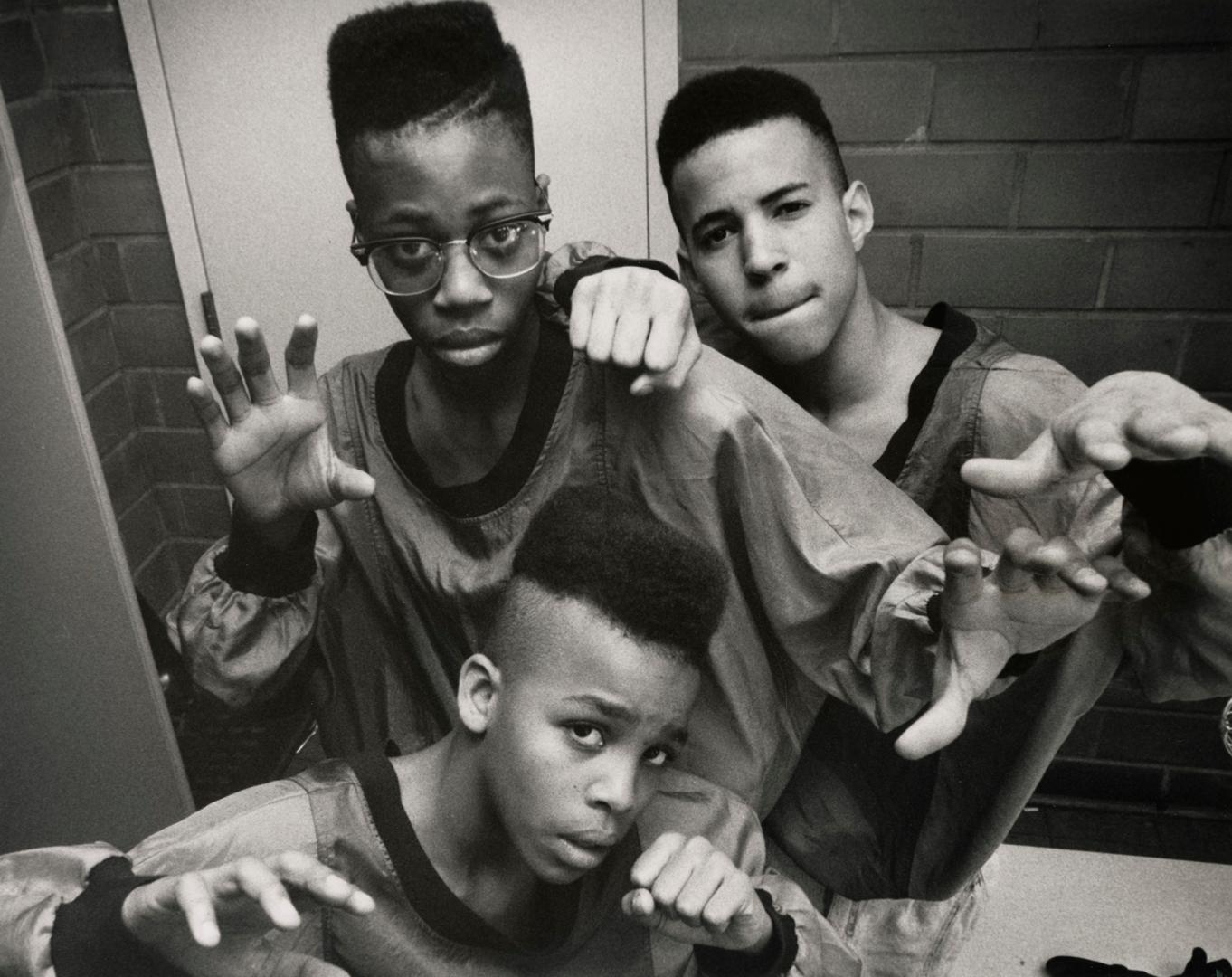 Three teen boys in matching t-shirts flex their arms in rapper style. 