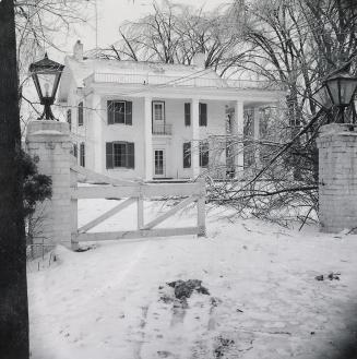 black and white photograph taken from the front gate of a two story house. 