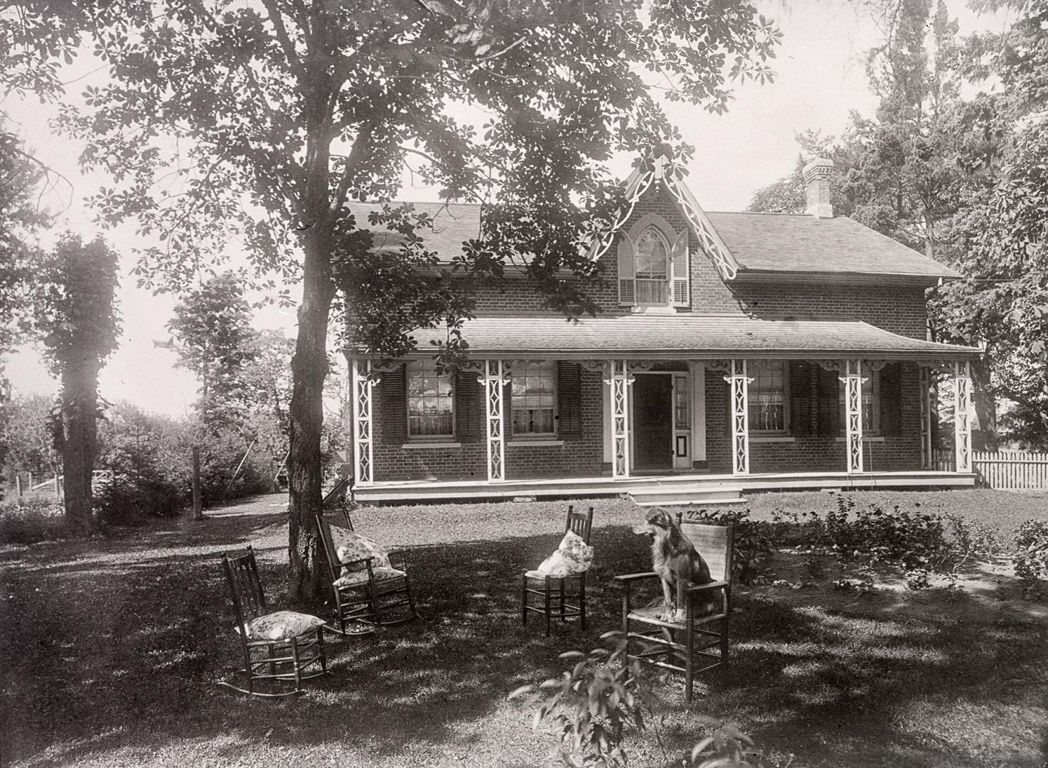 Black and white photo negative of a house. Facing the camera in front of the house are four cha…