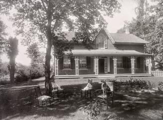 Black and white photo negative of a house. Facing the camera in front of the house are four cha…