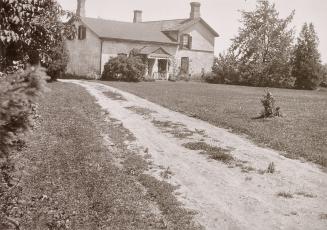 Black and white negative of a house at the end of a dirt path.