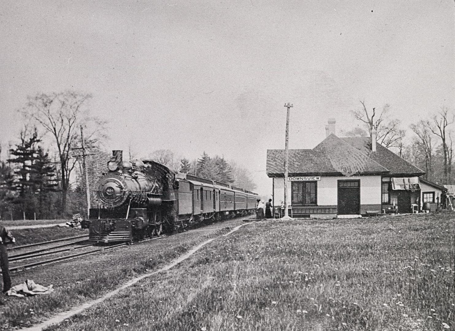 Black and white negative of a train stopped in front of a train station building.