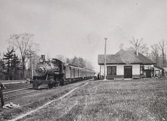 Black and white negative of a train stopped in front of a train station building.