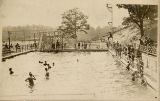 Black and white photograph of people swimming in a large pool.