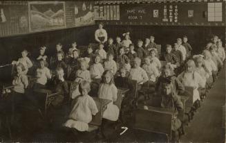 Black and white photograph of seated school children and their teacher in their classroom.
