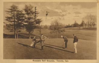Sepia-toned postcard depicting a golf course with four men in the forefront playing golf. The c ...