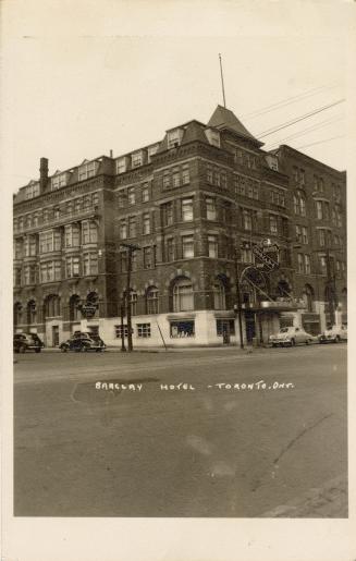 Black and white photo postcard depicting the exterior of a hotel on a street corner, with capti ...